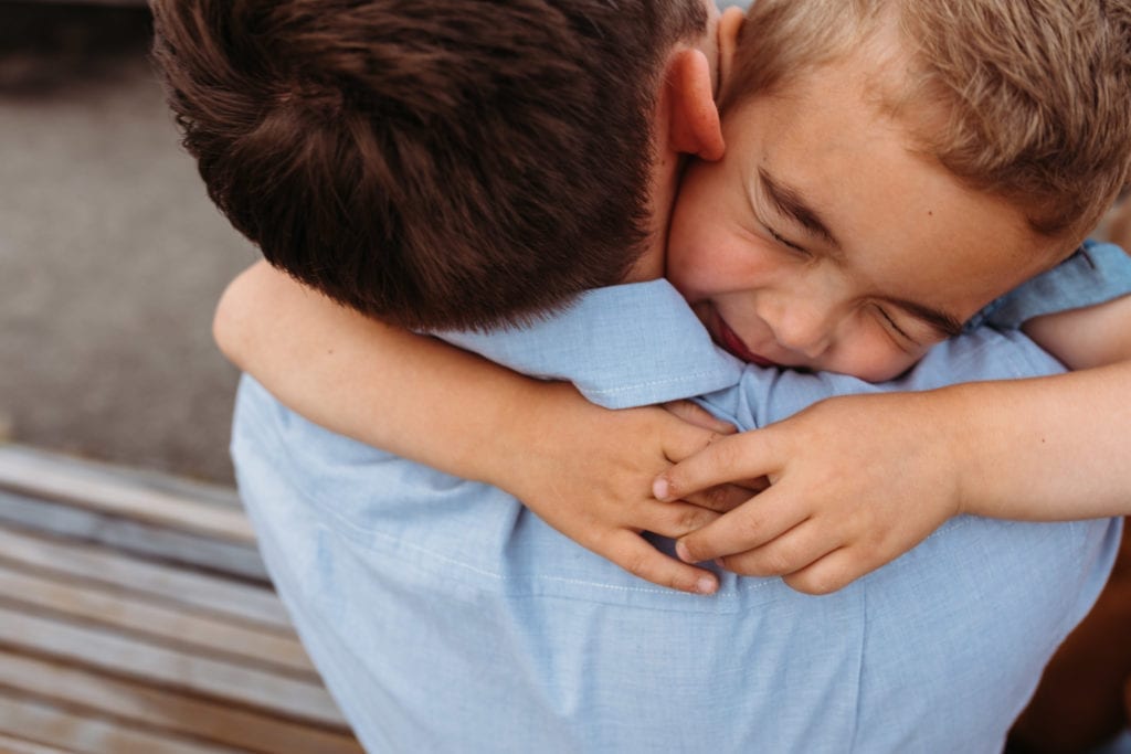 A boy is hugging his dad tightly. 