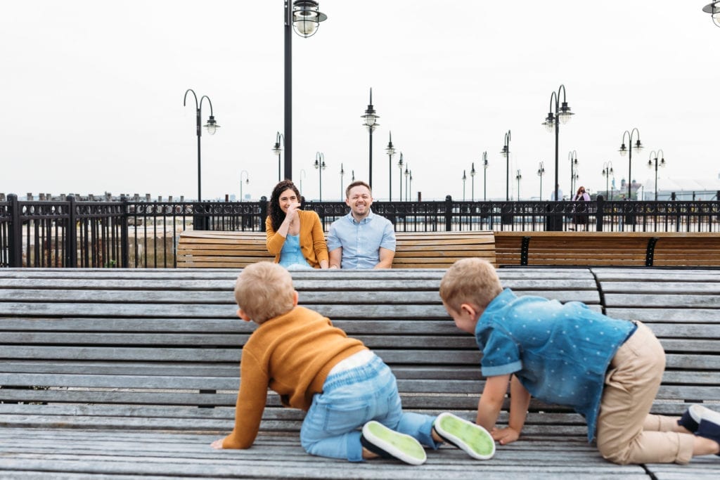 Two brothers are sneaking up on their mom and dad at a family photo session in Liberty State Park, NJ