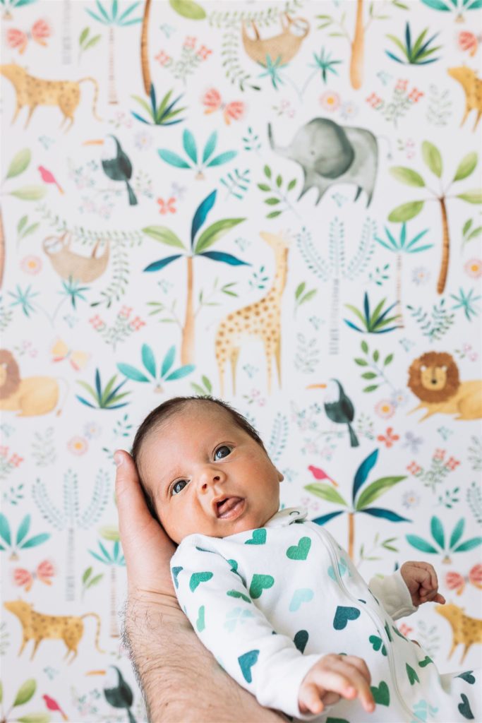 newborn baby held up to a colorful wallpaper in brooklyn nyc for a lifestyle newborn photo session