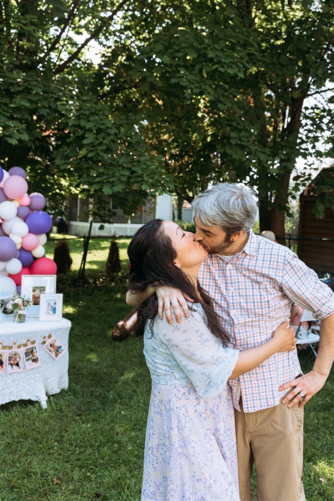 mom and dad enjoying a kiss during their child's first birthday party in westchester ny backyard