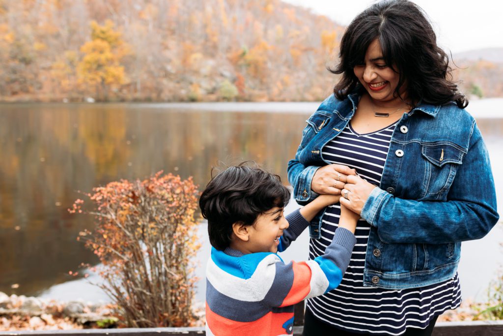 Fall maternity photo of a mother to be and her older son as they celebrate her growing baby bump at a one of the best NYC city parks for outdoor family photos surrounded by the changing colors of the fall season